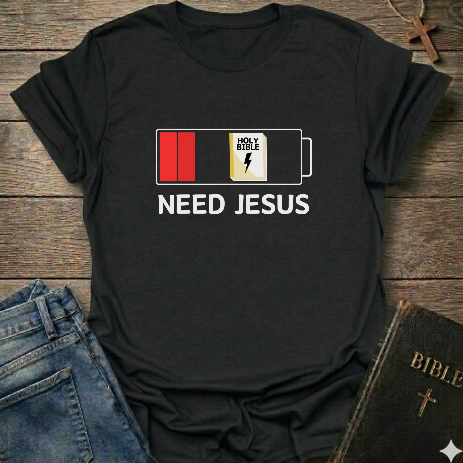 Black t-shirt with 'Need Jesus' graphic on a wooden surface with jeans and a Bible. Need Jesus to Recharge My Battery Christian T-Shirt bold faith apparel Faith Forward