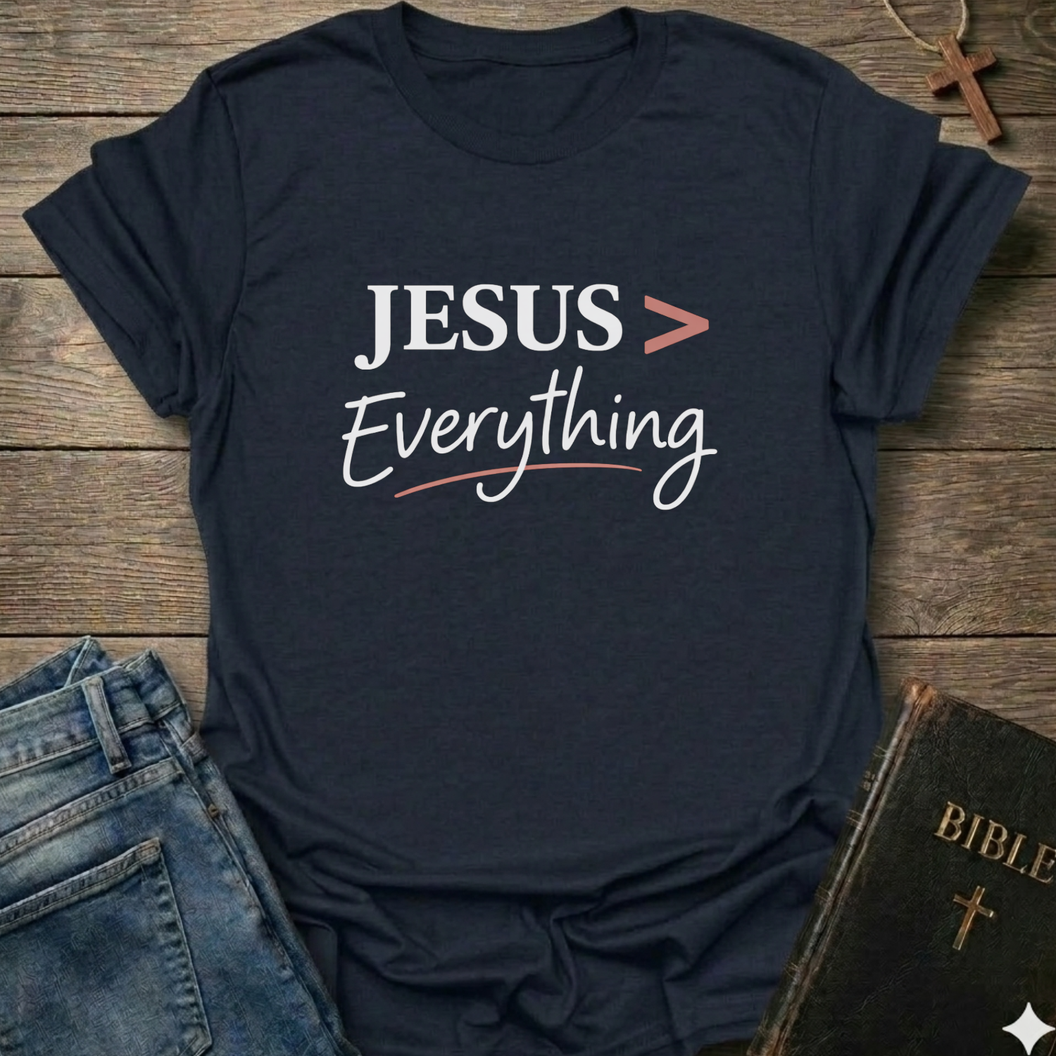 Navy blue T-Shirt faith apparel conversation starter with 'JESUS > Everything' text on a wooden surface with jeans and a Bible.