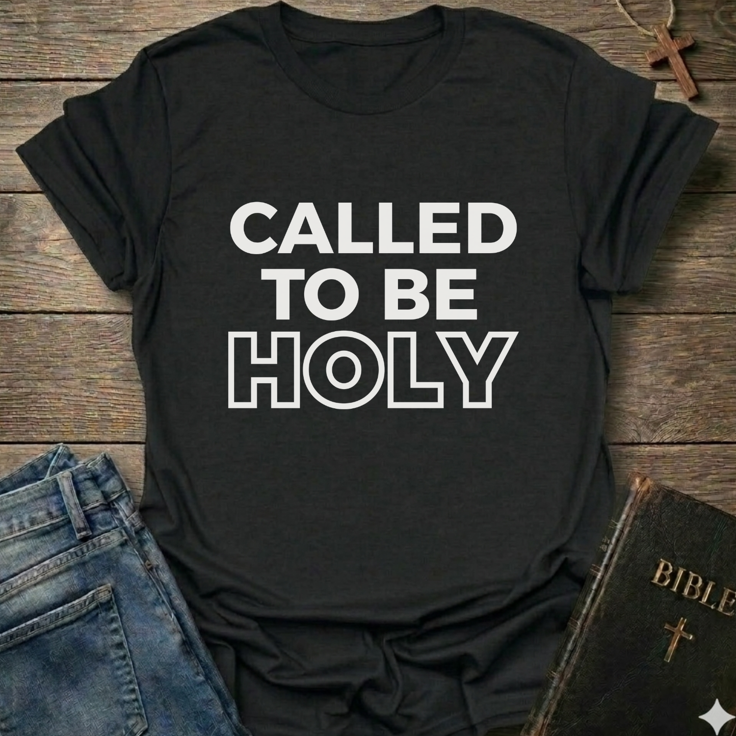 Black t-shirt with 'Called to be Holy' Christian T-Shirt bold faith apparel 1 Peter 1:15 conversation starter text on a wooden surface with jeans and a Bible.