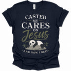 A navy blue short-sleeve t-shirt with a graphic print on the front. The print features the text 'CASTED MY CARES ON Jesus AND NOW I REST' in white and olive green lettering, along with an illustration of a sleeping panda resting on a rock with bamboo leaves.