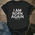 Navy blue t-shirt with with 'I AM BORN AGAIN 1 PETER 1:23' text I Am Born Again Christian bold faith apparel conversation starter on a wooden surface with jeans and a Bible.