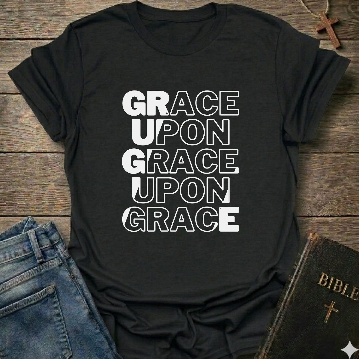 Black t-shirt with 'GRACE UPON GRACE UPON GRACE' Christian T-Shirt John 1:16 bold faith apparel text on a wooden surface with jeans and a Bible.