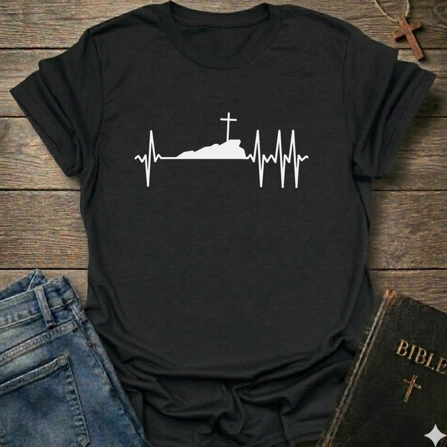 Black T-shirt with a white graphic design Cross Heartbeat Lifeline Christian minimal faith apparel conversation starter on a wooden surface with jeans and a Bible.