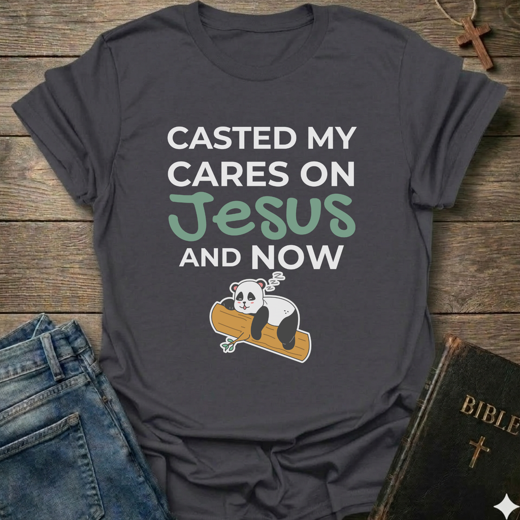 Gray t-shirt Casted My Cares on Jesus Christian relatable faith apparel conversation starter with a panda graphic and text on a wooden surface with jeans and a Bible.