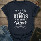 Navy blue t-shirt with white text "It is Not for Kings to Drink Wine" and 2 wine bottles graphic based on Proverbs 31:4 Christian faith apparel conversation starter on a wooden surface with jeans and a Bible.