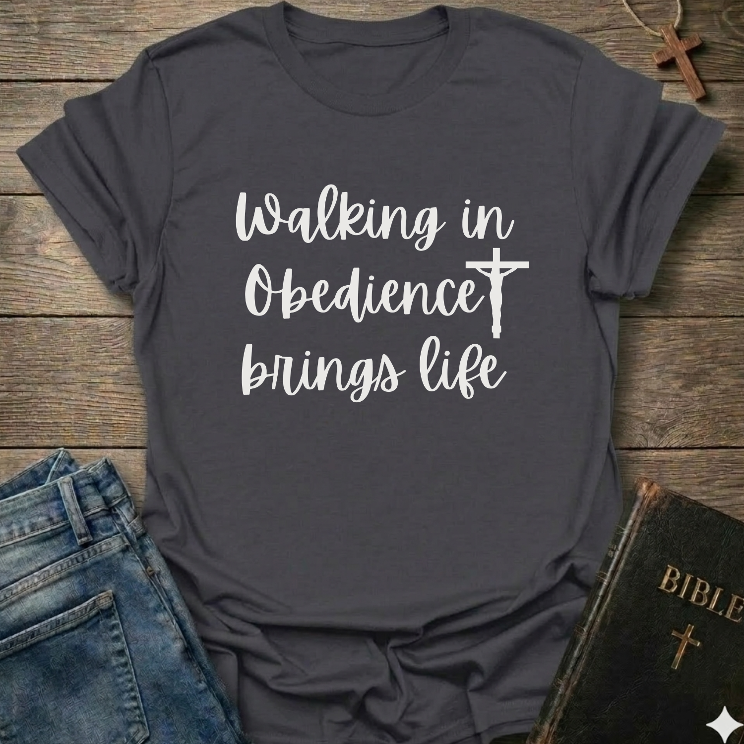 Gray t-shirt with 'Walking in Obedience brings life' text and cross graphic Christian script faith apparel conversation starter on a wooden surface.