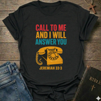 Black t-shirt with with vintage phone graphic and text Call to Me and I Will Answer You Jeremiah 33:3 retro phone faith Christian apparel conversation starter on a wooden surface with jeans and a Bible.