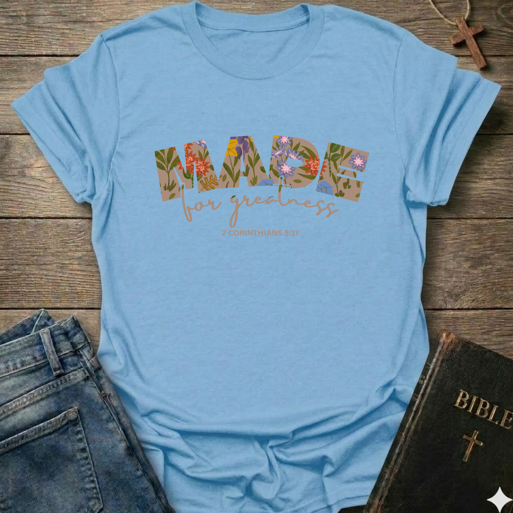 Light blue t-shirt with floral text design on a wooden surface with jeans and a Bible. Made for Greatness Christian T-Shirt 2 Corinthians 5:17 bold faith apparel Faith Forward women