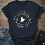 A navy blue graphic t-shirt laid flat on a rustic wooden surface, styled with blue jeans, a Bible, and a wooden cross. The t-shirt features a white circular graphic with a dove in the center and the words 'Fruit of Holy Spirit' in yellow, surrounded by white words including 'PATIENCE', 'KINDNESS', 'GOODNESS', 'FAITH', 'LOVE', 'JOY', 'PEACE', and 'GENTLENESS'.