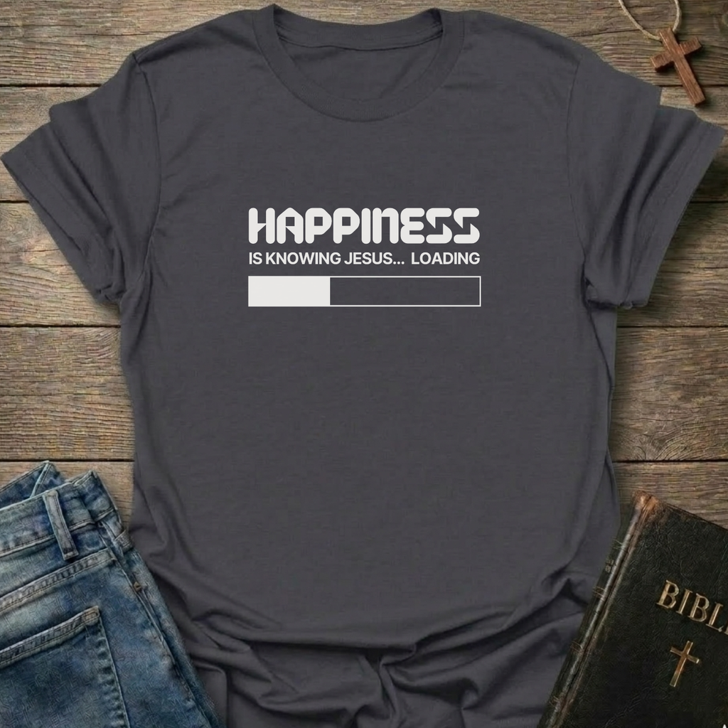 A dark gray graphic t-shirt  laid flat on a rustic wooden surface, styled with blue jeans and a Bible. The t-shirt features a white printed loading bar "like a battery charging" graphic that reads 'HAPPINESS IS KNOWING JESUS.