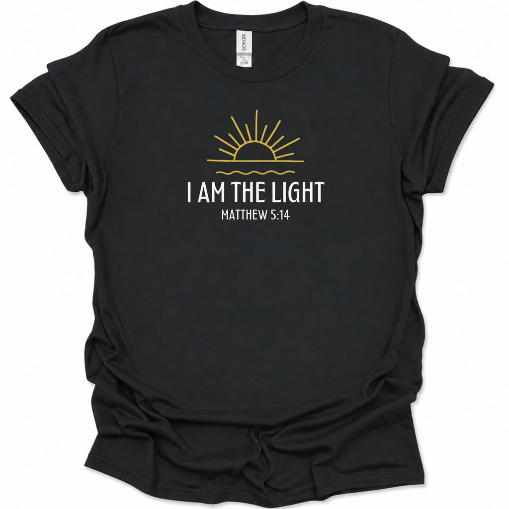 A black short-sleeve t-shirt with a graphic print on the front featuring a yellow rising sun and the text 'I AM THE LIGHT MATTHEW 5:14' in white, displayed on a clean white background.