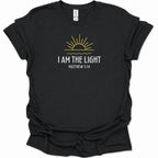 A black short-sleeve t-shirt with a graphic print on the front featuring a yellow rising sun and the text 'I AM THE LIGHT MATTHEW 5:14' in white, displayed on a clean white background.