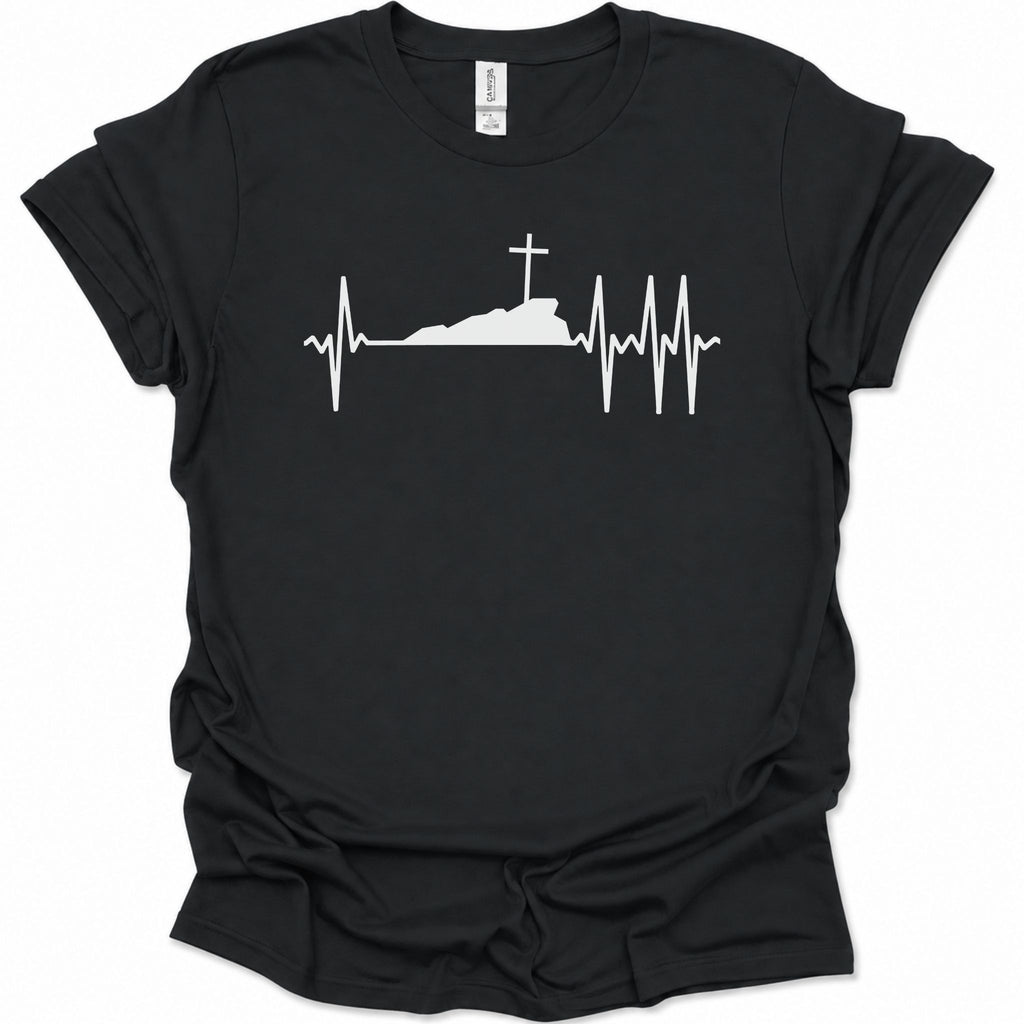 A black short-sleeve crewneck t-shirt with a white graphic print of a cross on top of a silhouette, integrated into an EKG heartbeat line, shown against a plain white background.