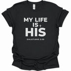 A black short-sleeve crewneck t-shirt with bold black text on the front reading 'MY LIFE IS + HIS' and 'GALATIANS 2:20' underneath, shown on a plain white background.