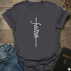 Dark gray t-shirt with 'faith' and cross design on a wooden surface with jeans and a Bible. Faith Minimalist Cross Script Christian T-Shirt bold faith apparel Faith Forward
