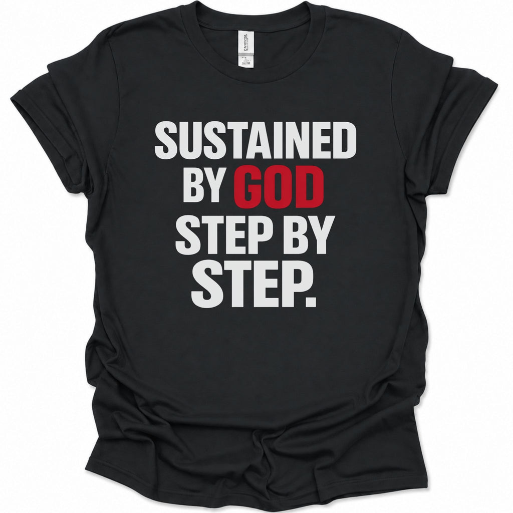 A black short-sleeve crewneck t-shirt with the text 'SUSTAINED BY GOD STEP BY STEP.' printed on the front in bold white and red letters, shown against a plain white background.