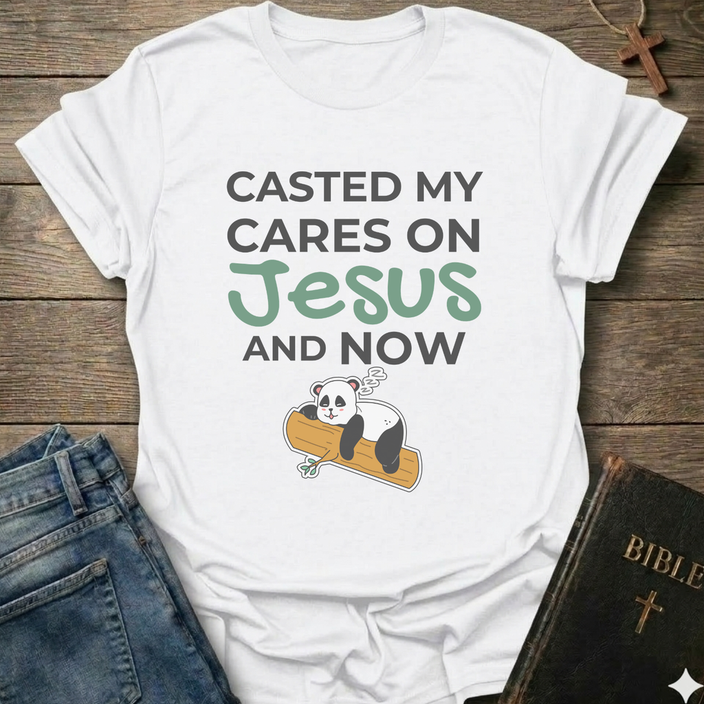 White t-shirt Casted My Cares on Jesus Christian relatable faith apparel conversation starter with a panda graphic and text on a wooden surface with jeans and a Bible.