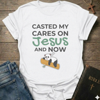White t-shirt Casted My Cares on Jesus Christian relatable faith apparel conversation starter with a panda graphic and text on a wooden surface with jeans and a Bible.