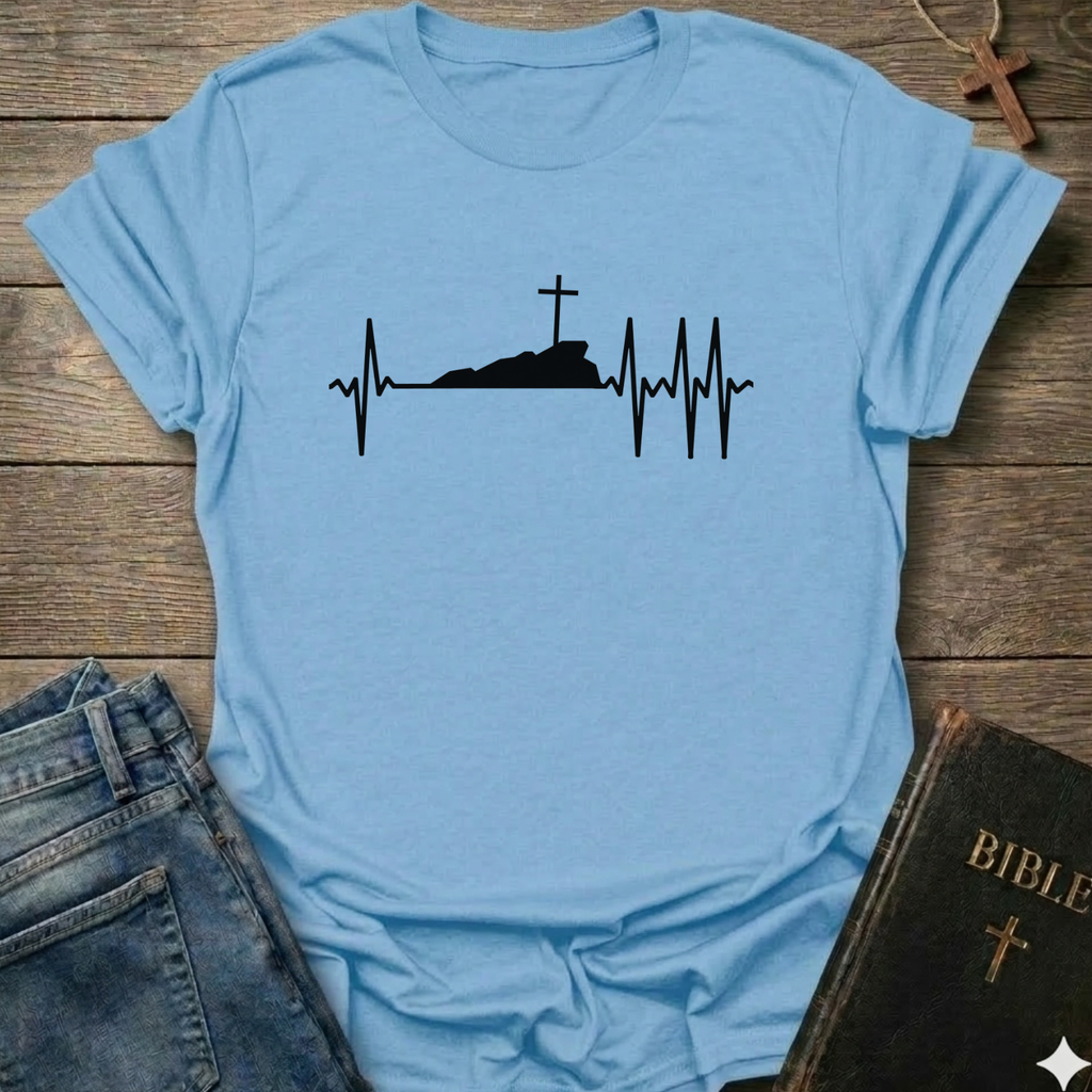 Light blue T-shirt with a white graphic design Cross Heartbeat Lifeline Christian minimal faith apparel conversation starter on a wooden surface with jeans and a Bible.