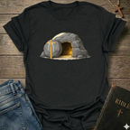 Black t-shirt with a graphic of a  Empty Tomb and a cross Christian resurrection faith apparel conversation starter on a wooden surface with jeans and a Bible.