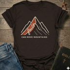 Dark brown Christian t-shirt with 'Faith can move mountains' graphic Matthew 17:20 faith apparel conversation starter on a wooden surface with jeans and a Bible. 