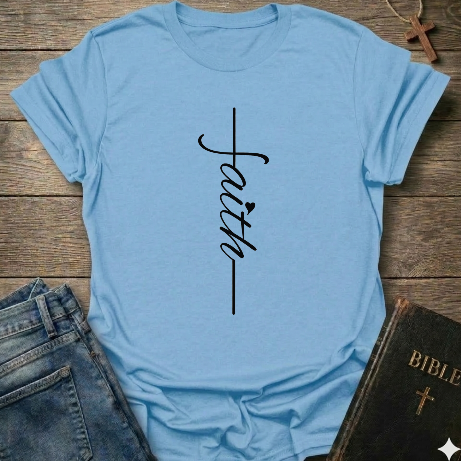 Light blue t-shirt with 'faith' printed on it, placed on a wooden surface with jeans and a Bible. Faith Minimalist Cross Script Christian T-Shirt bold faith apparel Faith Forward