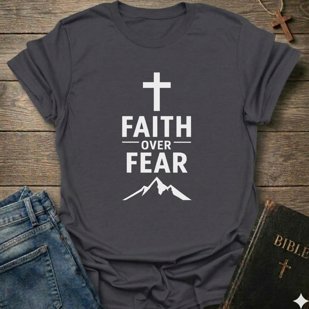 Gray t-shirt with 'Faith Over Fear' Cross Mountain Christian faith apparel conversation starter design on a wooden surface with jeans and a Bible.