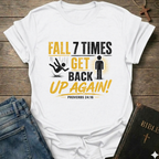 White t-shirt with motivational quote "Fall 7 Times Get Back Up Again Proverbs 24:16" bold graphic faith apparel Faith Forward on a wooden surface with jeans and a Bible.