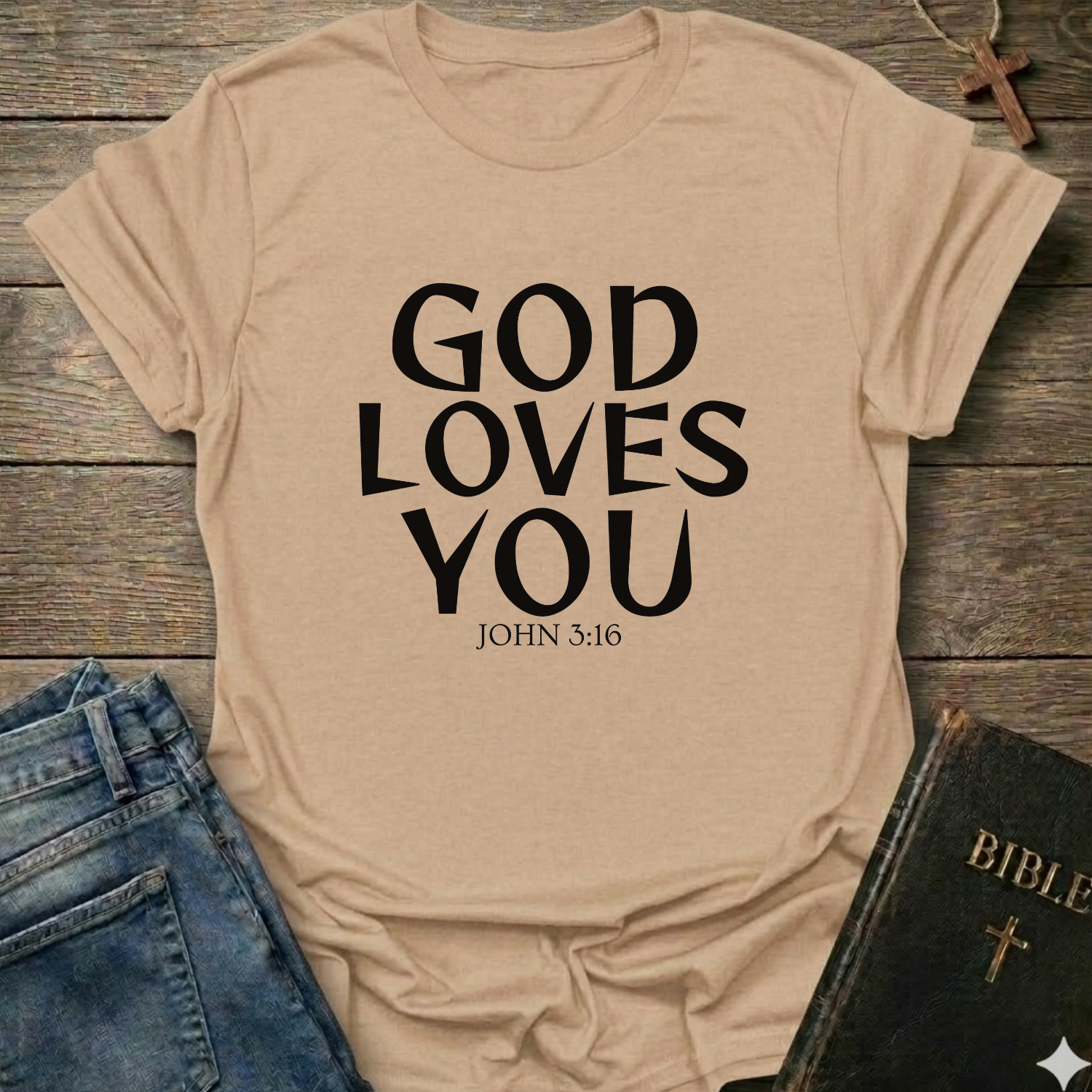 Natural t-shirt with 'GOD LOVES YOU' John 3:16 text Christian bold faith apparel Faith Forward on a wooden surface with jeans and a Bible.