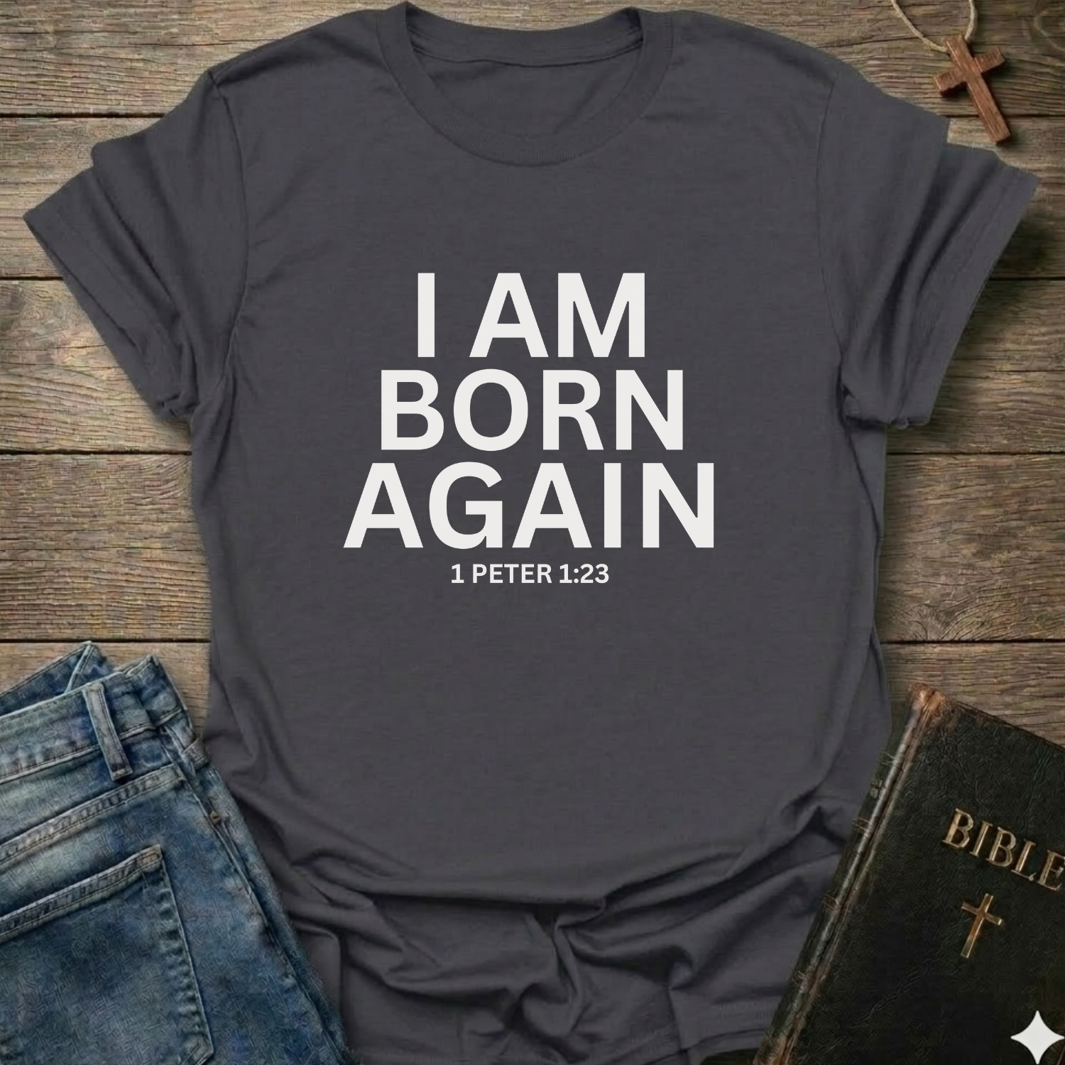 Dark gray t-shirt with 'I AM BORN AGAIN 1 PETER 1:23' text I Am Born Again Christian bold faith apparel conversation starter on a wooden surface with jeans and a Bible.