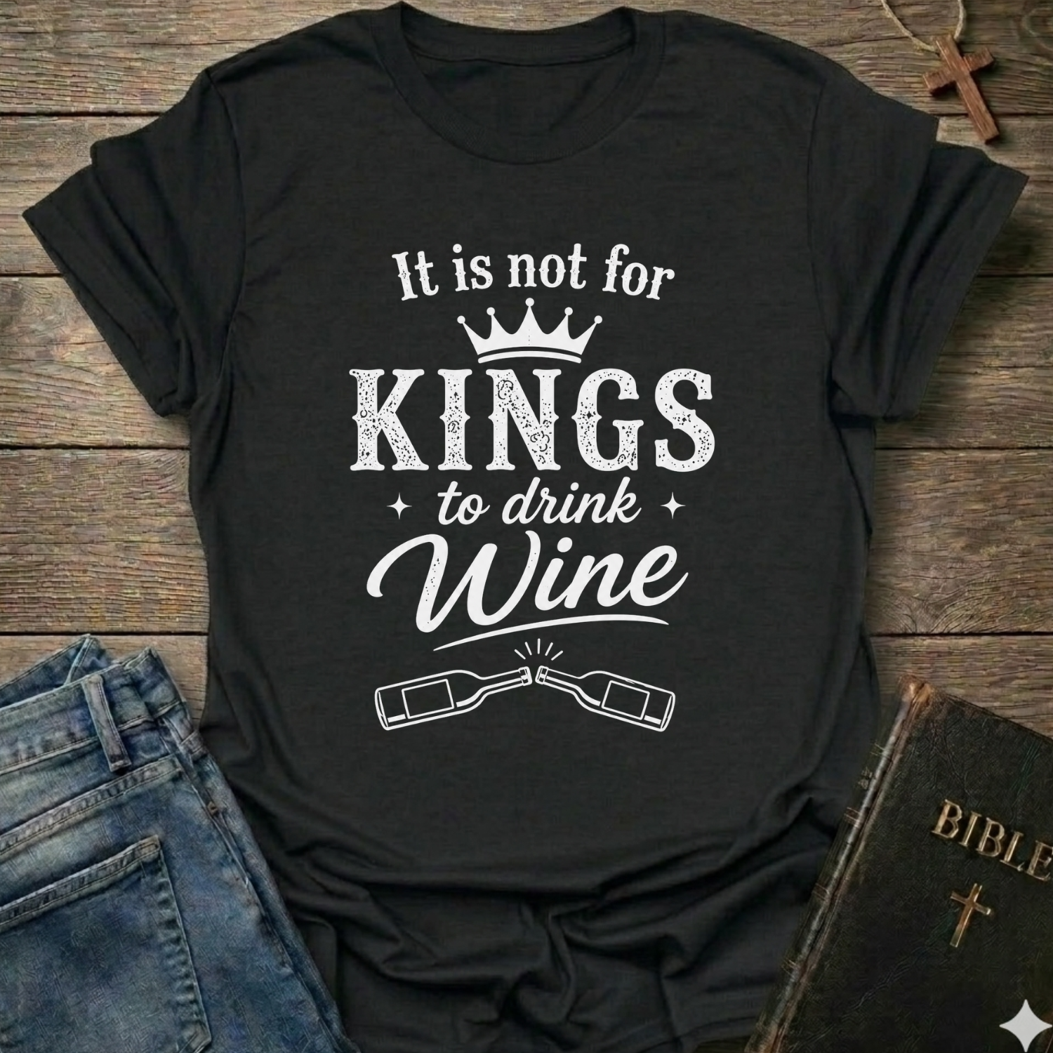 Black t-shirt with white text "It is Not for Kings to Drink Wine" and 2 wine bottles graphic based on Proverbs 31:4 Christian faith apparel conversation starter on a wooden surface with jeans and a Bible.