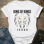 White t-shirt with 'King of Kings Jesus Lion Cross Revelation 19:16 faith apparel conversation starter' on a wooden surface. 