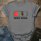 Gray t-shirt with 'Need Jesus' graphic on a wooden surface with jeans and a Bible. Need Jesus to Recharge My Battery Christian T-Shirt bold faith apparel Faith Forward