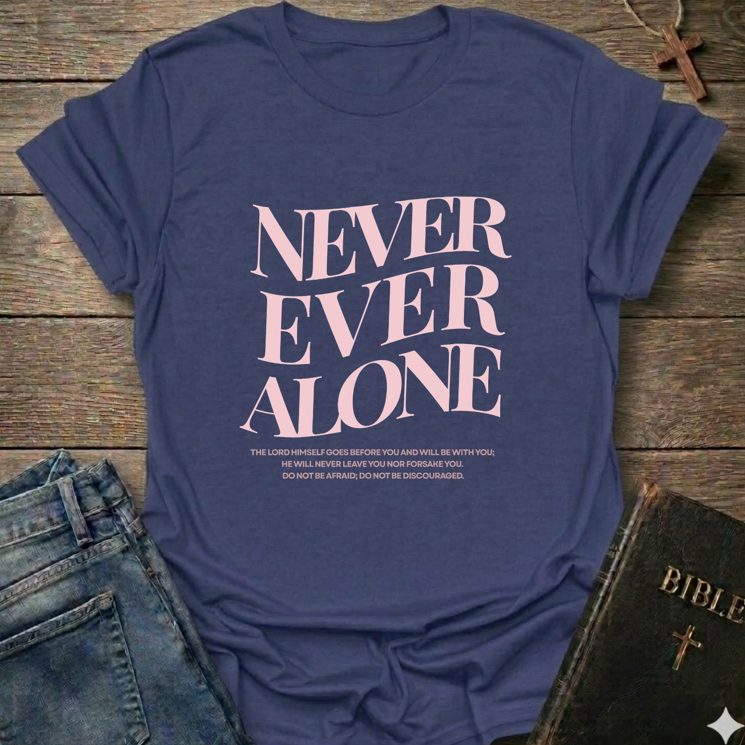 Purple t-shirt with 'NEVER EVER ALONE' text on a wooden surface with jeans and a Bible. Never Ever Alone Never Forsaken Christian T-Shirt Deuteronomy 31:8 bold faith apparel Faith Forward