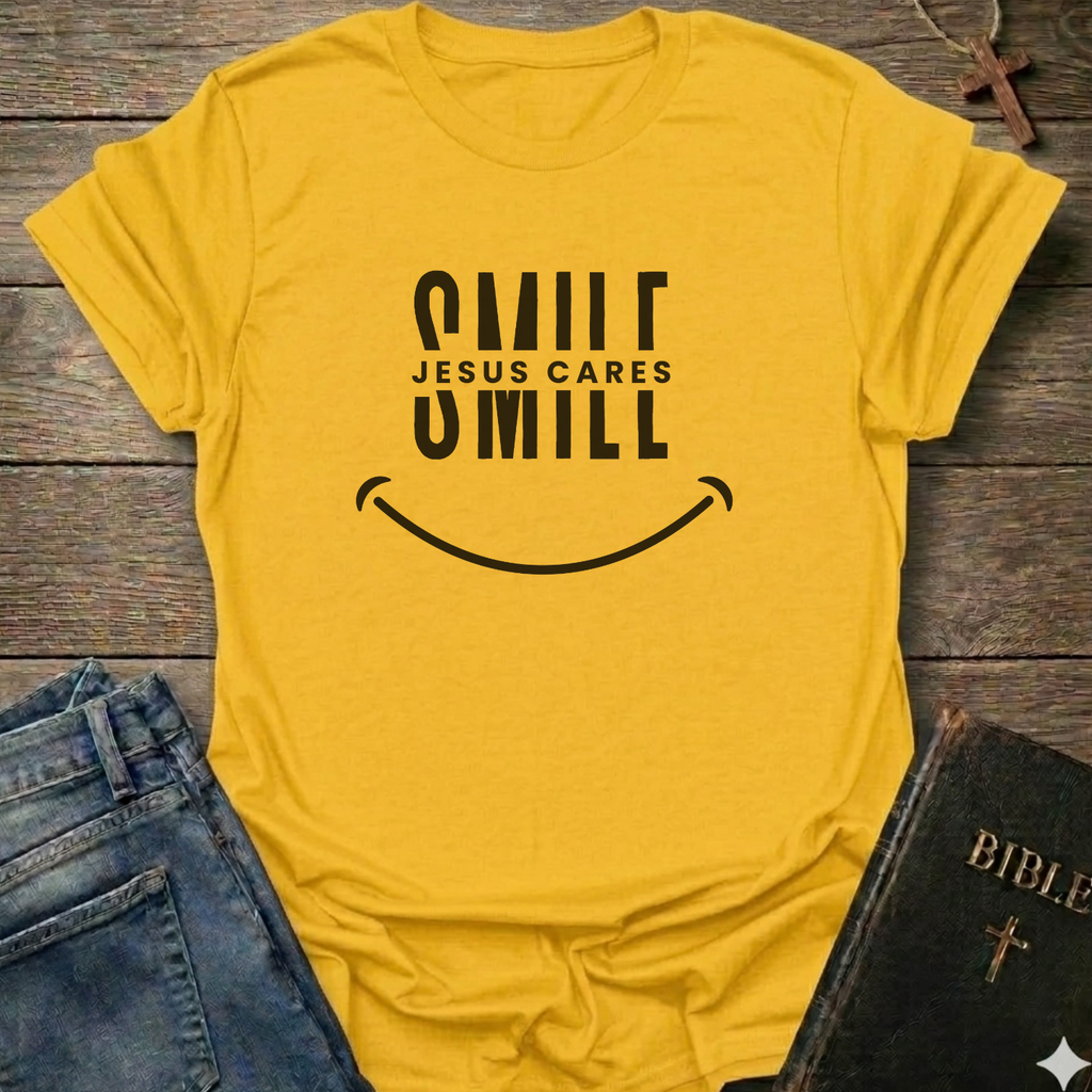 A yellow short-sleeve t-shirt with a black graphic reading 'SMILE JESUS CARES SMILL' and a smiley face, styled flat on a rustic wooden surface with blue jeans and a Bible nearby.