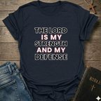 Navy blue t-shirt with 'The Lord is my strength and my defense' Exodus 15:2 bold faith apparel Faith Forward on a wooden surface with jeans and a Bible.