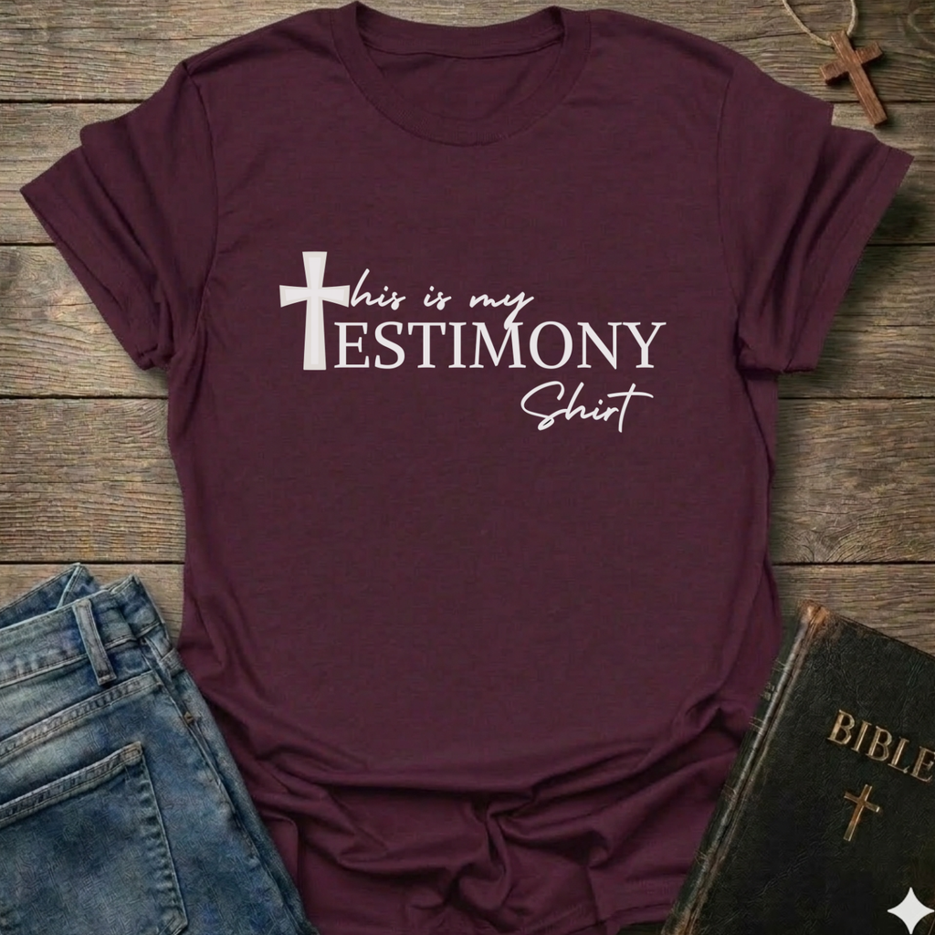 Maroon t-shirt with 'This is my testimony shirt' text and cross minimal faith apparel conversation starter. It is on a wooden surface with jeans and a Bible.