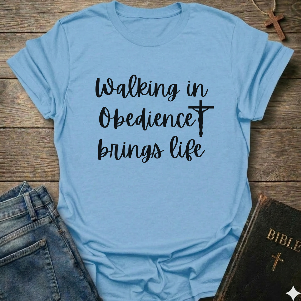 Light blue t-shirt with 'Walking in Obedience brings life' text and cross graphic Christian script faith apparel conversation starter on a wooden surface.